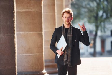 Ellerinde dizüstü bilgisayarla. Dost canlısı, gözlüklü, zarif bir genç şehirde resmi şık kıyafetler giyiyor..