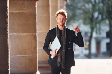 Ellerinde dizüstü bilgisayarla. Dost canlısı, gözlüklü, zarif bir genç şehirde resmi şık kıyafetler giyiyor..