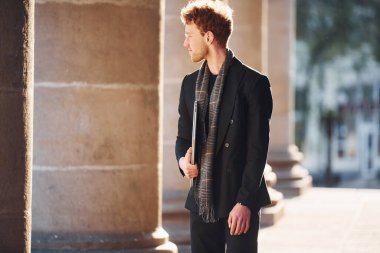 Ellerinde dizüstü bilgisayarla. Dost canlısı, gözlüklü, zarif bir genç şehirde resmi şık kıyafetler giyiyor..