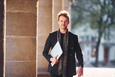 Ellerinde dizüstü bilgisayarla. Dost canlısı, gözlüklü, zarif bir genç şehirde resmi şık kıyafetler giyiyor..