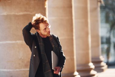 Ellerinde dizüstü bilgisayarla. Dost canlısı, gözlüklü, zarif bir genç şehirde resmi şık kıyafetler giyiyor..