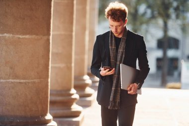 Dizüstü bilgisayar ve telefon ellerindeyken. Gözlüklü zarif genç adam şehrin dışında şık kıyafetler giyiyor..
