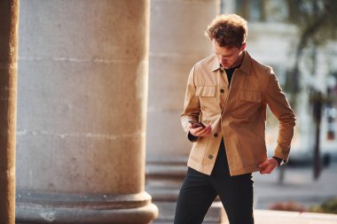 Telefonu elimde tutuyorum. Şehrin dışında şık kıyafetler içinde zarif bir genç adam..