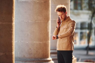 Talking by phone. Elegant young man in formal classy clothes outdoors in the city.