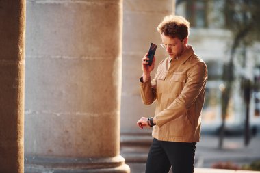 Telefonla konuşuyorum. Şehrin dışında şık kıyafetler içinde zarif bir genç adam..