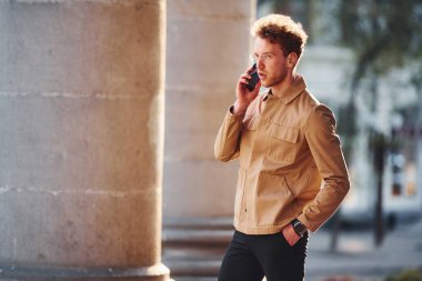 Telefonla konuşuyorum. Şehrin dışında şık kıyafetler içinde zarif bir genç adam..