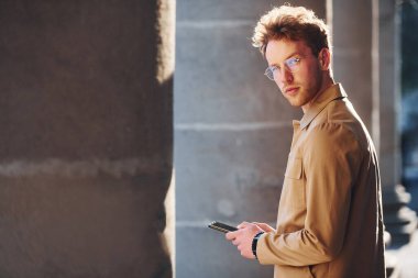 Güzel gün ışığı. Telefonu elimde tutuyorum. Şehrin dışında şık kıyafetler içinde zarif bir genç adam..