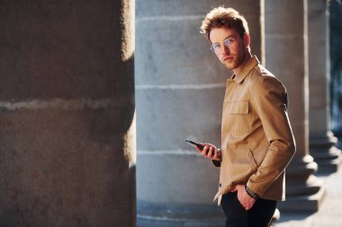 Güzel gün ışığı. Telefonu elimde tutuyorum. Şehrin dışında şık kıyafetler içinde zarif bir genç adam..