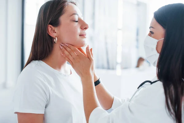 Checking lymph nodes and throat. Young woman have a visit with female doctor in modern clinic.