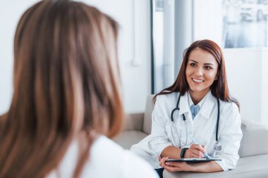 Oturup konuşmak. Genç bayan, modern klinikteki kadın doktoru ziyaret ediyor..