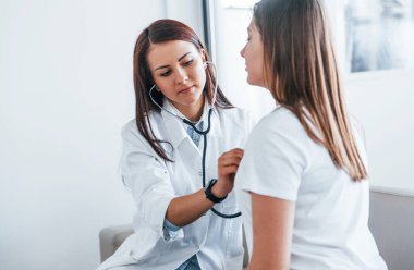 Steteskop kullanıyorum. Genç bayan, modern klinikteki kadın doktoru ziyaret ediyor..
