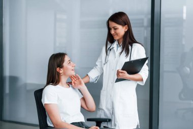 Friendly doctor listening to the patient. Young woman have a visit with female doctor in modern clinic. clipart