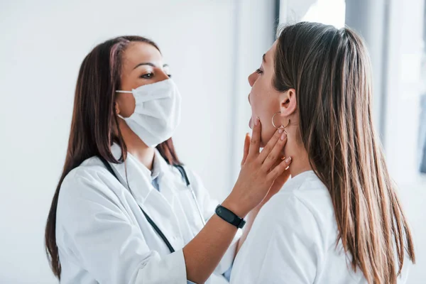 Checking lymph nodes and throat. Young woman have a visit with female doctor in modern clinic.