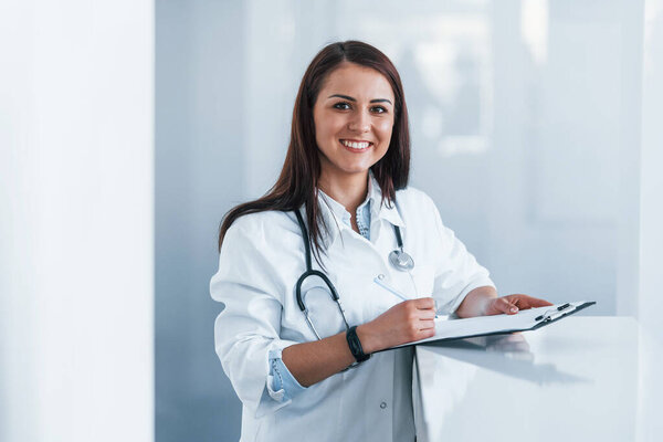 С блокнотом. Молодая медсестра в помещении современной клиники. Концепция здравоохранения.