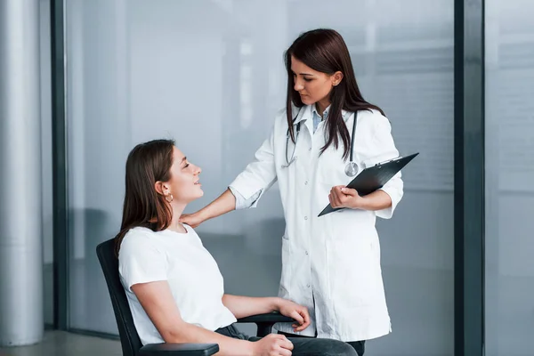 Friendly doctor listening to the patient. Young woman have a visit with female doctor in modern clinic.