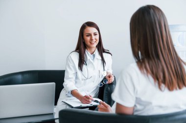 Oturup konuşmak. Genç bayan, modern klinikteki kadın doktoru ziyaret ediyor..