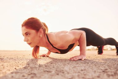 Woman in sportswear doing push-ups on the road at evening time.
