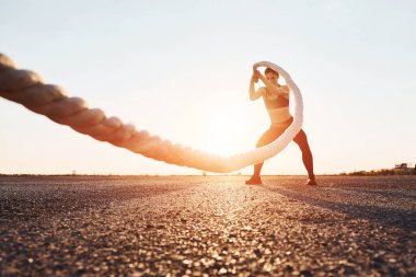 Woman in sportswear training with knots on the road at evening time.