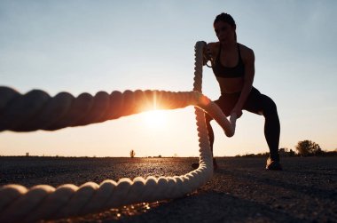 Spor giyimli bir kadın akşam vakti yolda düğümlerle antrenman yapıyor..