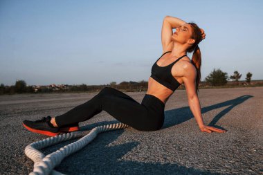 Spor kıyafetli bir kadın akşam vakti yolda düğümlerle oturuyor..