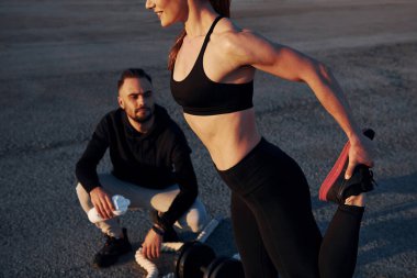 Adam oturur ve elinde bir şişe su tutar. Kadın ve erkeğin akşam vakti yolda spor günleri olur..