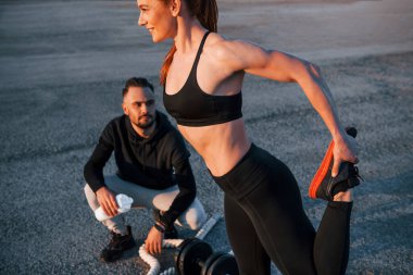 Adam oturur ve elinde bir şişe su tutar. Kadın ve erkeğin akşam vakti yolda spor günleri olur..