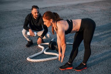 Adam oturur ve elinde bir şişe su tutar. Kadın ve erkeğin akşam vakti yolda spor günleri olur..