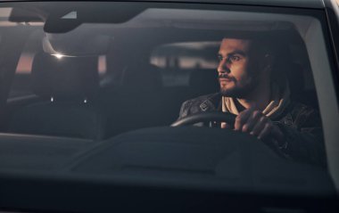 Moda giysileri içinde arabasıyla gezen yakışıklı, tıraşsız bir adamın ön görüntüsü..