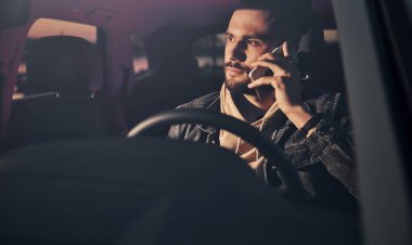 Moda kıyafetleri içinde, arabasıyla gezen ve telefonla konuşan yakışıklı, tıraşsız bir adamın ön görüntüsü..