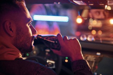 Siyah ve kırmızı polis ışıkları. İçkili araba kullanma. Arabasının içinde şık giyinmiş, tıraşsız, yakışıklı bir adam..