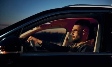 Arabasına binen şık giyinmiş, tıraşsız yakışıklı adamın yan görüntüsü..