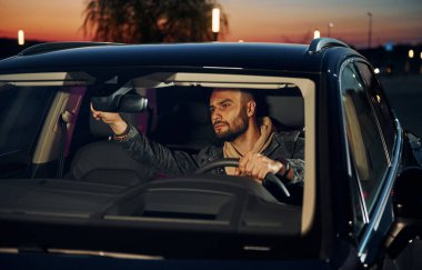 Şık giyinmiş, traşsız yakışıklı bir adam otomobiline biniyor..