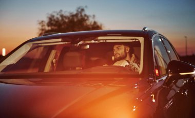 Şık giyinmiş, traşsız yakışıklı bir adam otomobiline biniyor..