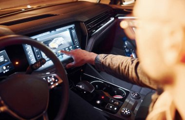 Navigasyon ekranı kullanılıyor. Şık giyinmiş, traşsız yakışıklı bir adam otomobiline biniyor..