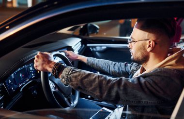 Navigasyon ekranı kullanılıyor. Şık giyinmiş, traşsız yakışıklı bir adam otomobiline biniyor..