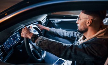 Navigasyon ekranı kullanılıyor. Şık giyinmiş, traşsız yakışıklı bir adam otomobiline biniyor..