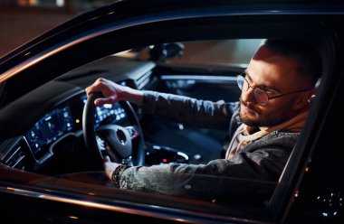 Arabasına binen şık giyinmiş, tıraşsız yakışıklı adamın yan görüntüsü..