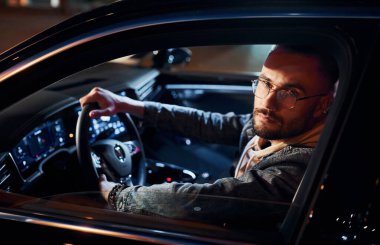 Arabasına binen şık giyinmiş, tıraşsız yakışıklı adamın yan görüntüsü..