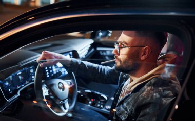 Arabasına binen şık giyinmiş, tıraşsız yakışıklı adamın yan görüntüsü..