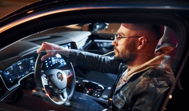 Arabasına binen şık giyinmiş, tıraşsız yakışıklı adamın yan görüntüsü..