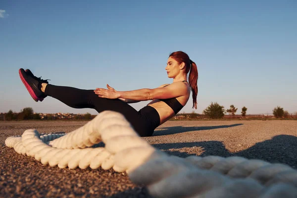 Spor kıyafetli bir kadın akşam vakti yolda düğümlerle oturuyor..