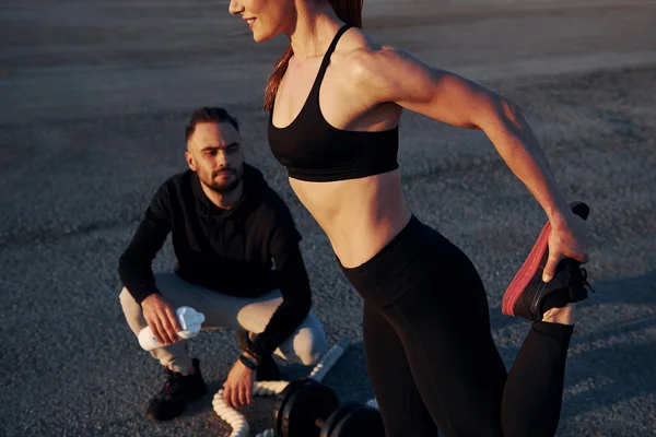 Adam oturur ve elinde bir şişe su tutar. Kadın ve erkeğin akşam vakti yolda spor günleri olur..