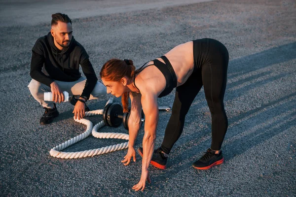 Adam oturur ve elinde bir şişe su tutar. Kadın ve erkeğin akşam vakti yolda spor günleri olur..