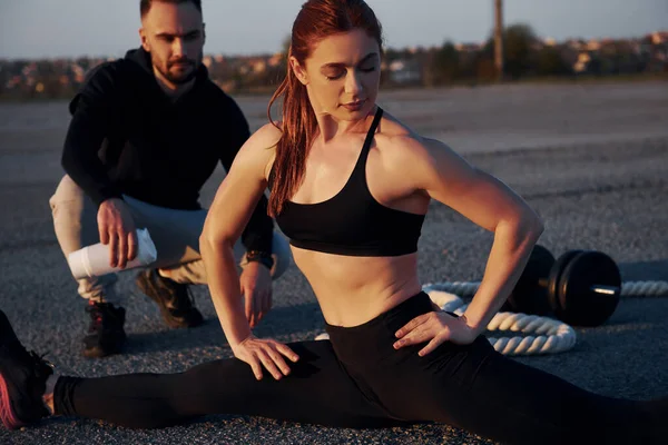 Adam oturur ve elinde bir şişe su tutar. Kadın ve erkeğin akşam vakti yolda spor günleri olur..