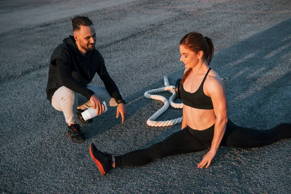 Adam oturur ve elinde bir şişe su tutar. Kadın ve erkeğin akşam vakti yolda spor günleri olur..