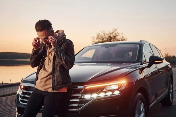 Yakışıklı, tıraşsız, siyah arabasında şık kıyafetler giyen bir adam..