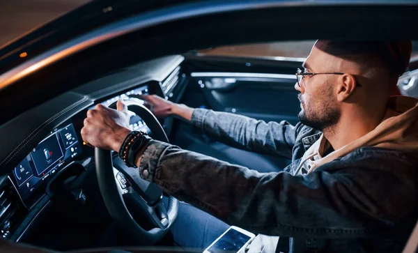 Navigasyon ekranı kullanılıyor. Şık giyinmiş, traşsız yakışıklı bir adam otomobiline biniyor..