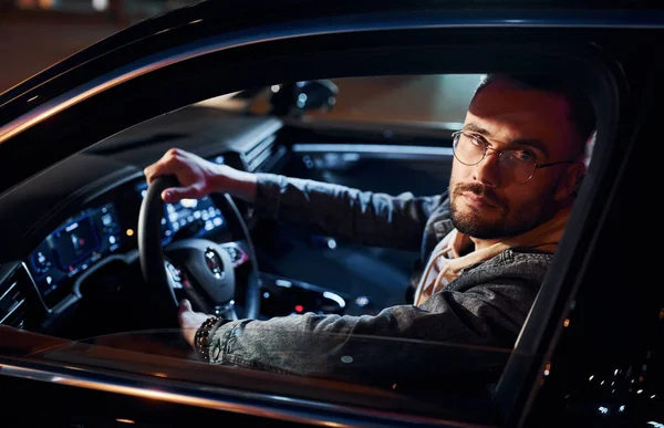 Arabasına binen şık giyinmiş, tıraşsız yakışıklı adamın yan görüntüsü..