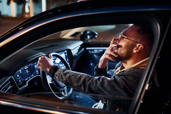 Şık giyinmiş, traşsız, yorgun ve yakışıklı bir adam otomobilini sürüyor..