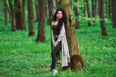 Siyah kotlu güzel esmer ağaçların yanında duruyor..